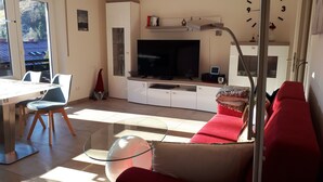 Ein modernes Wohnzimmer mit Fernseher, Sofa und Essbereich.