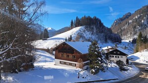 Eine Holzhütte mit schneebedecktem Dach, eingebettet in eine verschneite Landschaft und Berge.