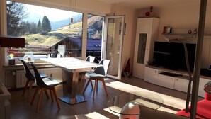 Eine moderne Küche mit Essbereich, großen Fenstern und Bergblick, einem Fernseher und einem Schrank mit Dekoration.