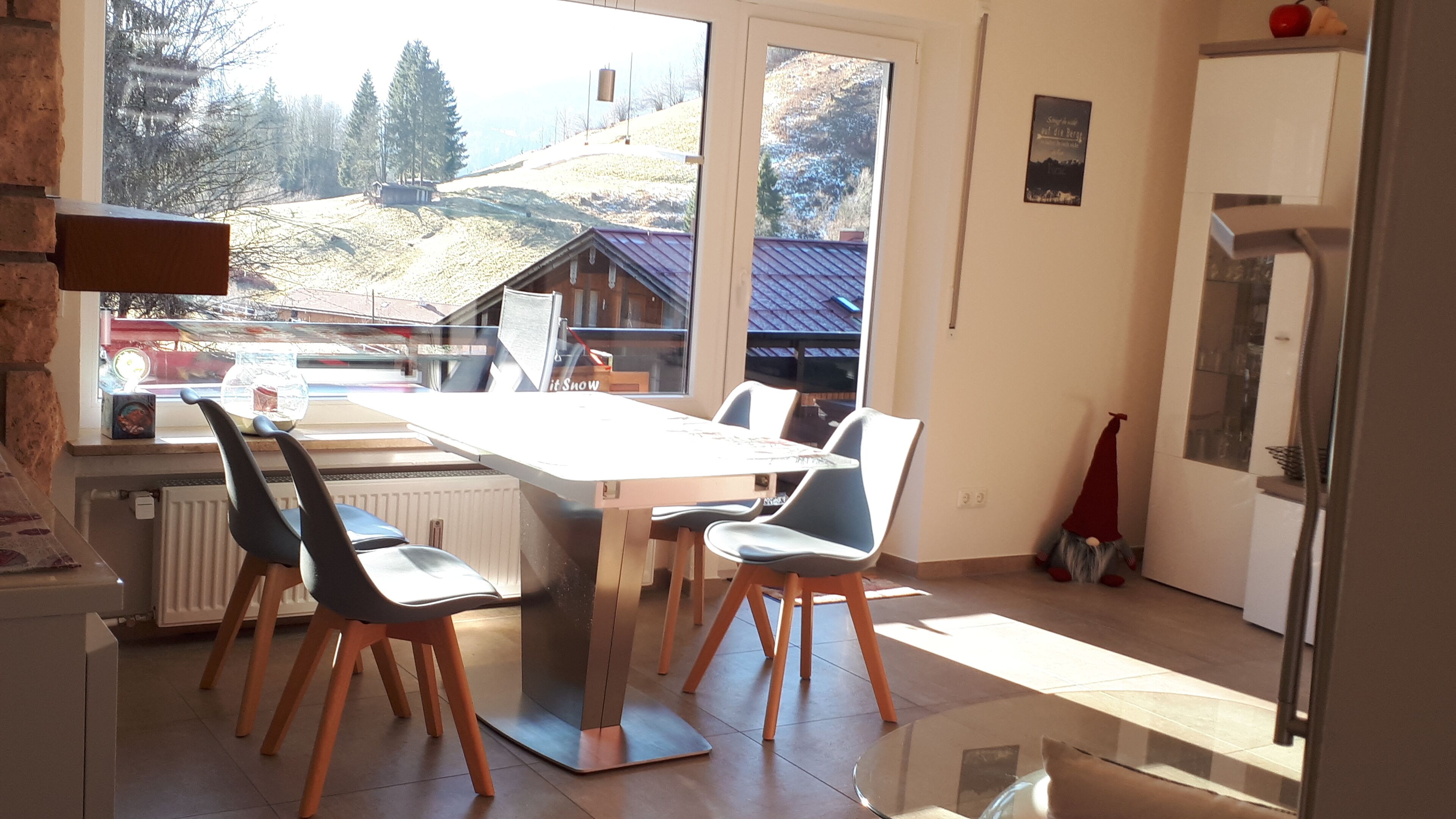 Un coin repas avec une table et des chaises, un radiateur et une vue sur un paysage enneigé par de grandes fenêtres.