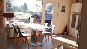Ein Essbereich mit Tisch und Stühlen, einem Heizkörper und Blick auf eine verschneite Landschaft durch große Fenster.