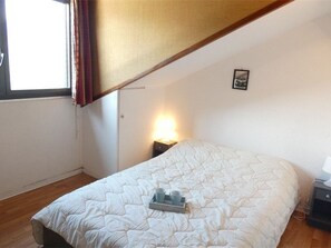 Une chambre à coucher avec un lit, une table de chevet, une fenêtre avec des rideaux et un petit tableau accroché au mur.
