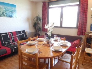 Un coin repas avec une table ronde en bois, dressée pour quatre personnes, entourée de chaises en bois.