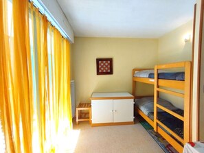 A small, single-room accommodation with a bunk bed, a small table, and a cabinet. - Charming 1BR Apartment, 6 Sleeps, Balcony, Near Gondolas, Parking, 2* Rating (Saint-Lary-Soulan)