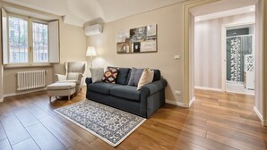 Un salon avec un canapé gris foncé, un tapis à motifs, un radiateur blanc et une fenêtre avec des rideaux.