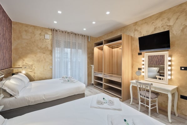 Une chambre d’hôtel avec deux lits, une coiffeuse avec un miroir et des lampes, une télévision et un dressing.