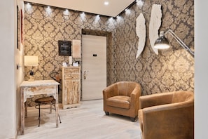 Une pièce avec un papier peint à motifs, un bureau avec une lampe, une chaise, un meuble et une porte.