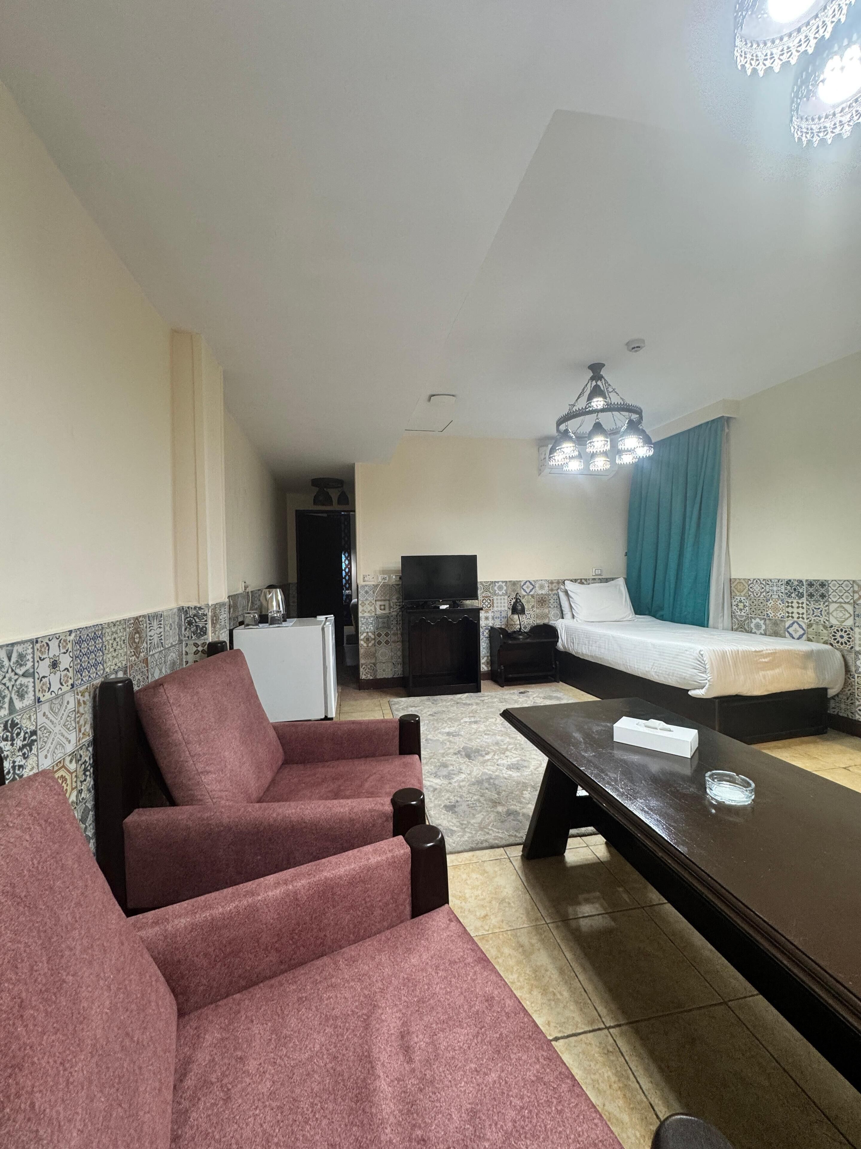 Una habitación con sofá, cama, televisión y candelabro.