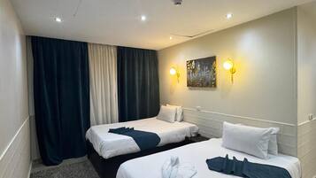 Une chambre d’hôtel avec deux lits, une moquette grise, un tableau au mur et un luminaire au plafond.