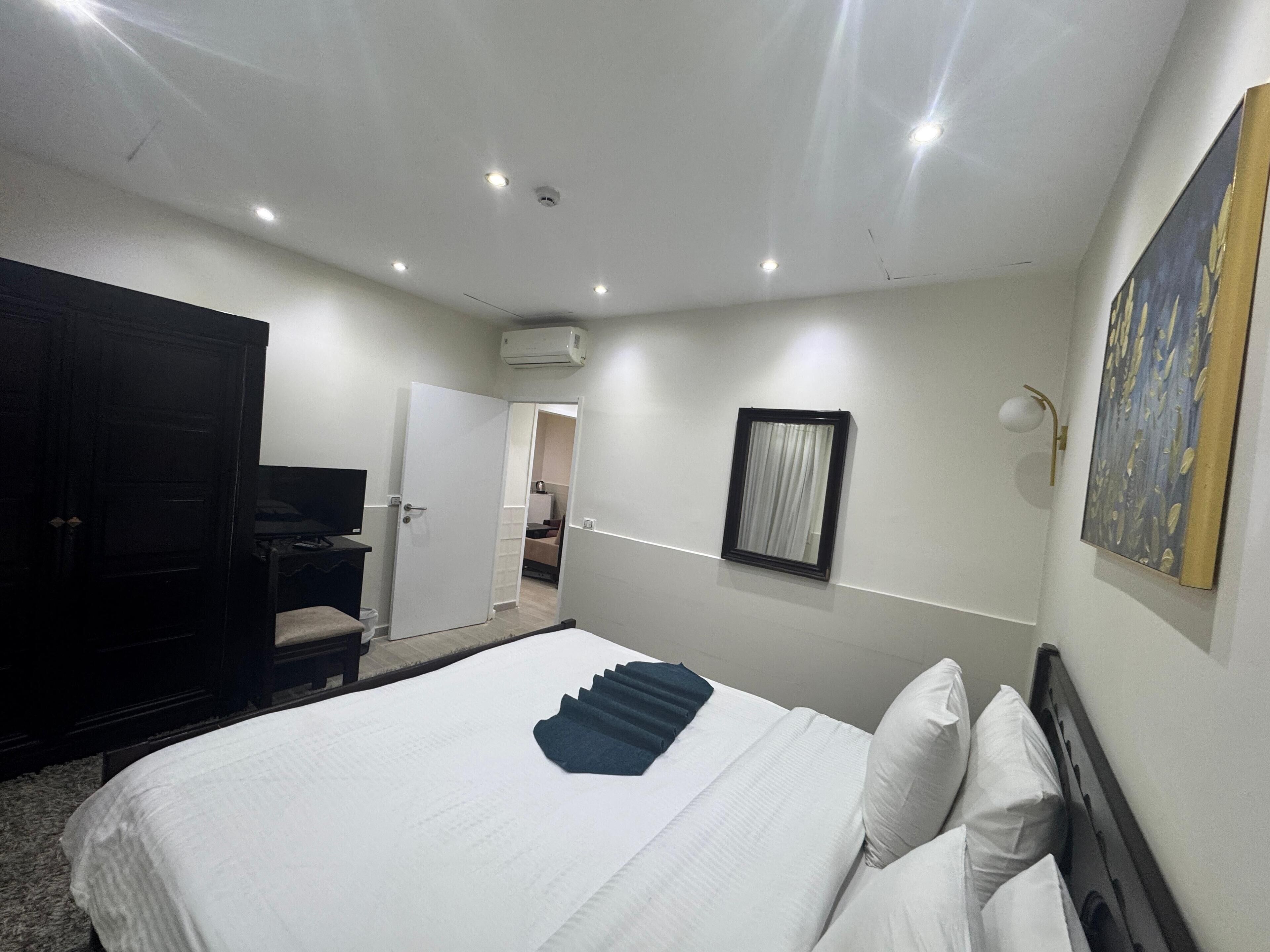 Habitació d'hotel amb un llit, una taula de treball, una cadira, un armari, un quadre i una porta que condueix a una altra habitació.