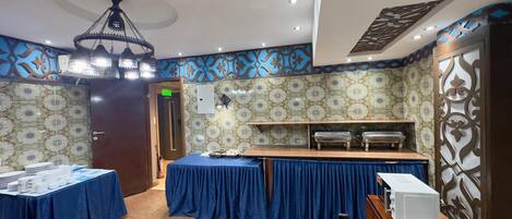 A room with patterned walls, a chandelier, a buffet setup, and a door leading to another area.