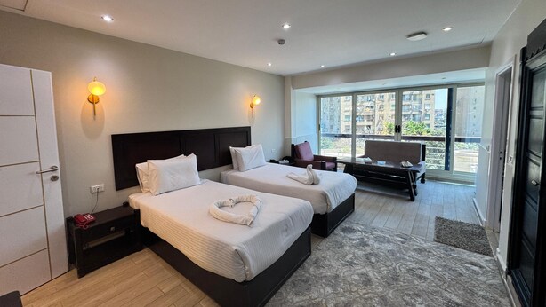 A hotel room with two beds, a desk, a chair, and a large window offering a city view. - New Star Zamalek Hotel (Cairo)