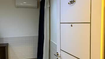 Een hotelkamer met een betegelde vloer, een witte inloopkast met nummerbord, een gordijn en een airconditioner aan de muur.