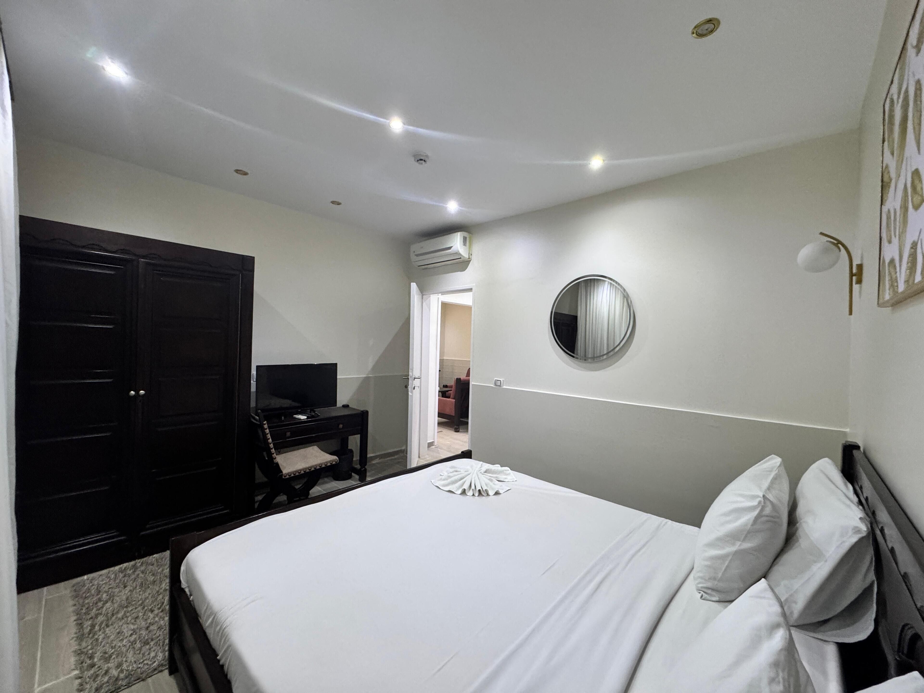 A bedroom with a bed, a desk, a wardrobe, and an air conditioning unit.