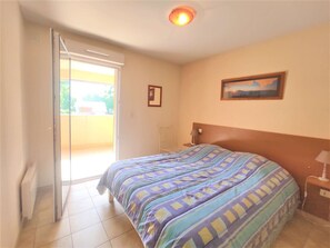 Quarto com cama, mesa de cabeceira, luminária, pintura na parede e porta de correr para uma varanda.