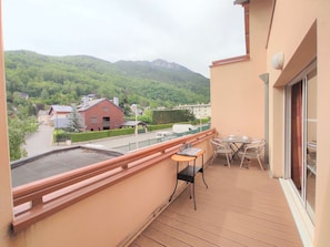 A balcony with a table and chairs, overlooking a residential area with houses and a mountain in the background.