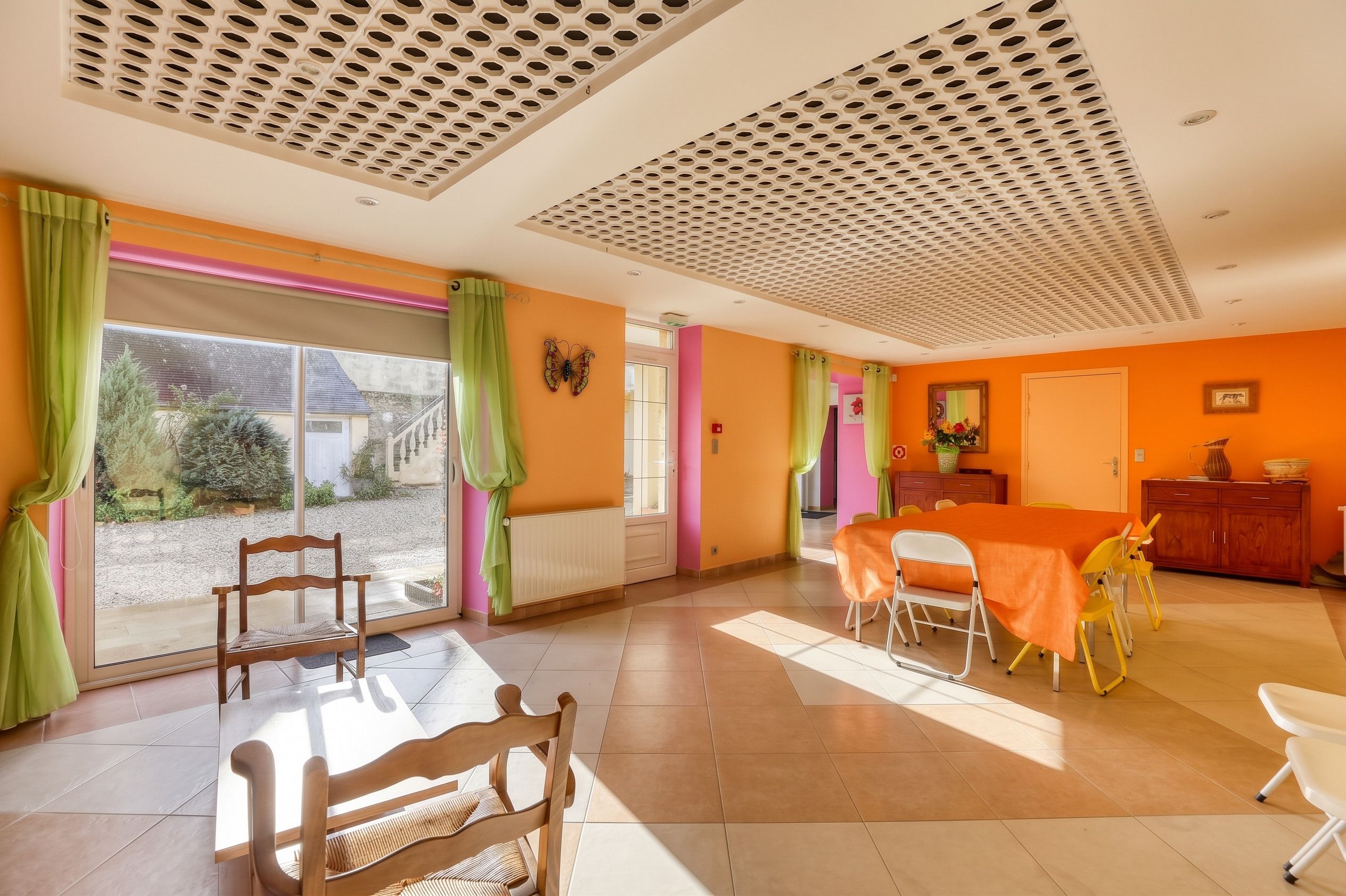 A dining area with a table and chairs, a window with curtains, and a ceiling with a perforated design.