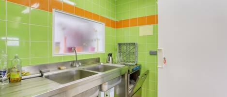 A kitchen with green and orange tiles, stainless steel appliances, and a window with frosted glass.