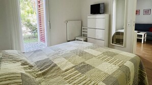 Ein Schlafzimmer mit Bett, Fernseher auf einer Kommode und Blick ins Freie durch eine Tür.