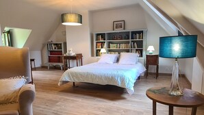 A bedroom with a bed, a chair, a table, a bookshelf, and a lamp.