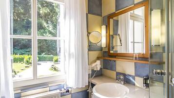 A bathroom with a large window, a round mirror, a sink, and a shower area.