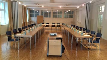 Uma sala de conferências com mesas compridas, cadeiras e um projetor.