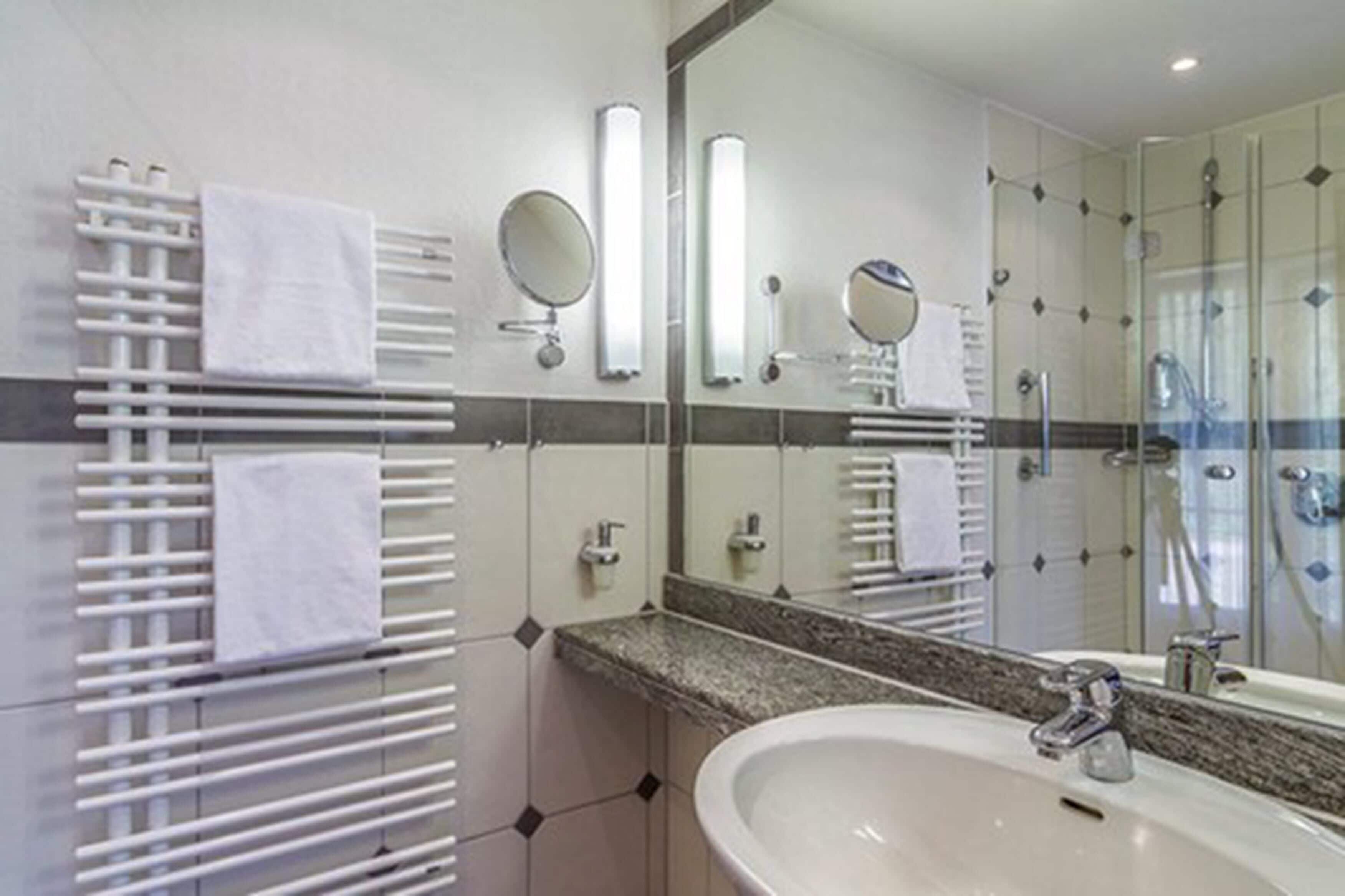 Un baño moderno con un espejo grande, encimera de granito, lavamanos blanco y cabina de ducha con paredes de vidrio.