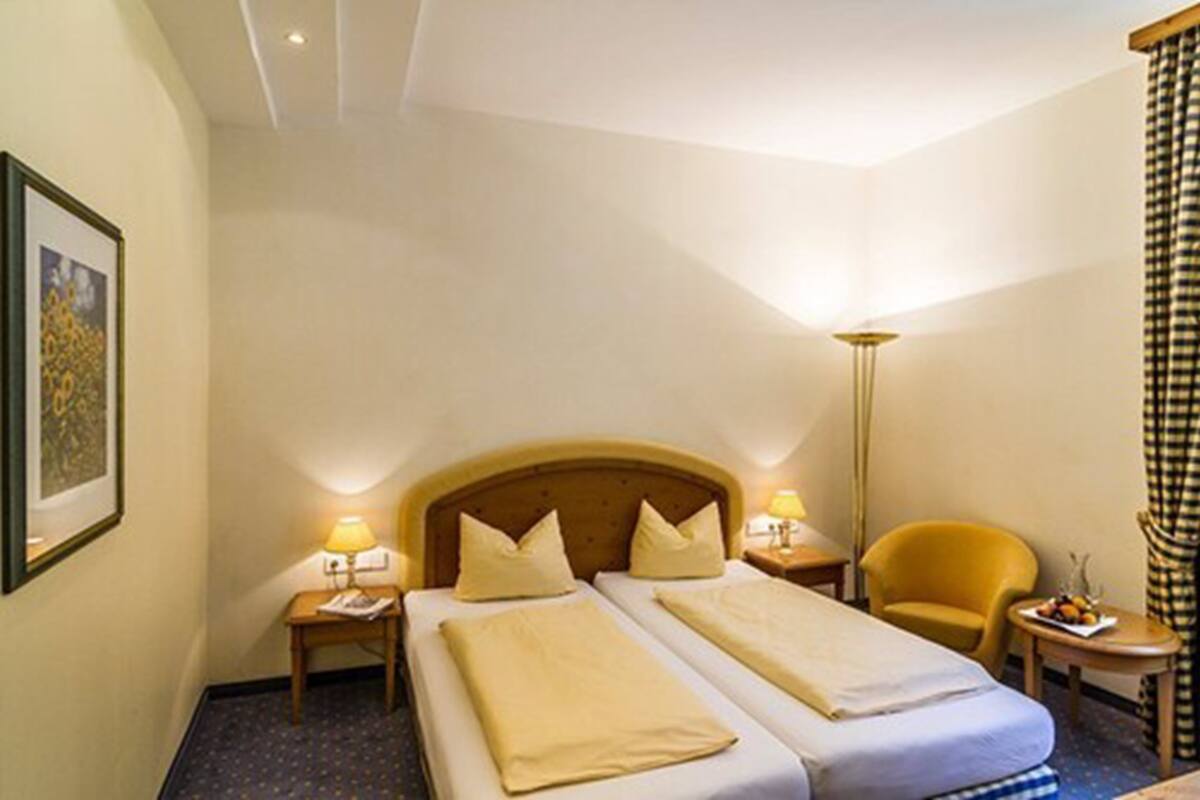 Une chambre d’hôtel avec deux lits, une table de chevet avec une lampe, une chaise et une petite table avec des fruits.