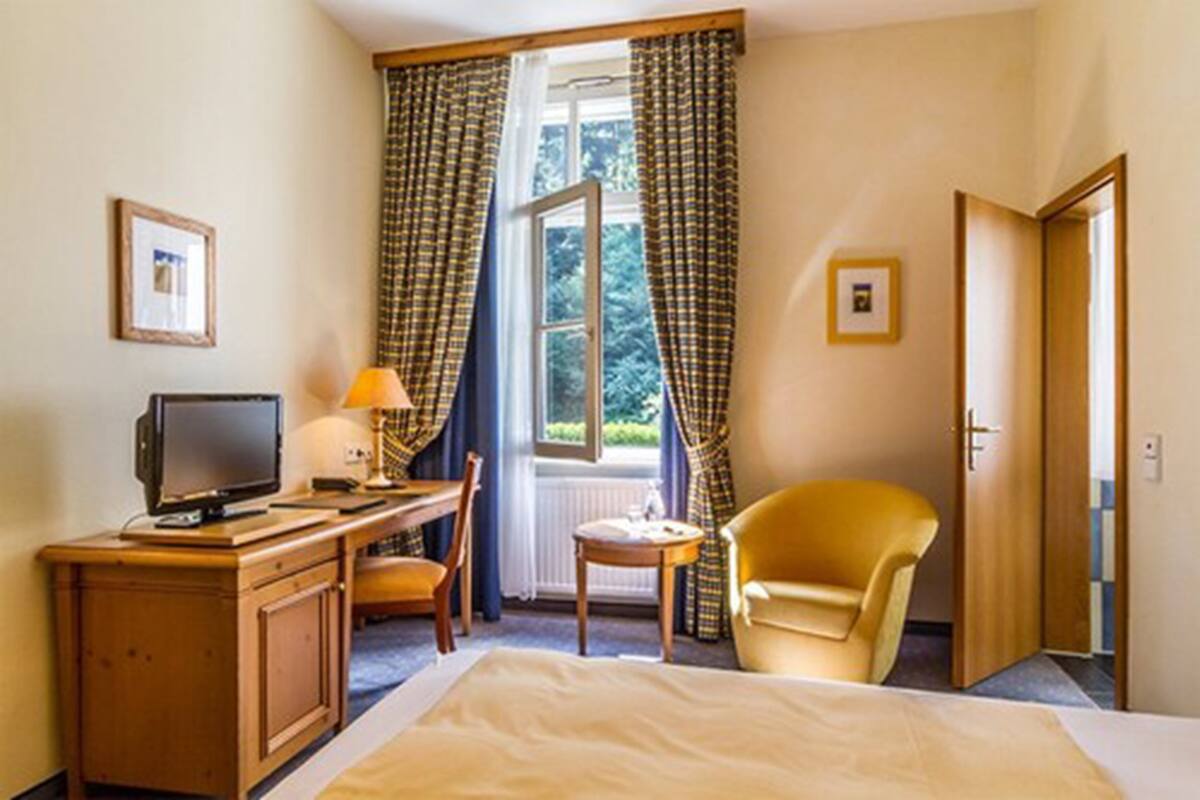 Une chambre d’hôtel avec un lit, un bureau avec un ordinateur, une chaise, une petite table et des rideaux.