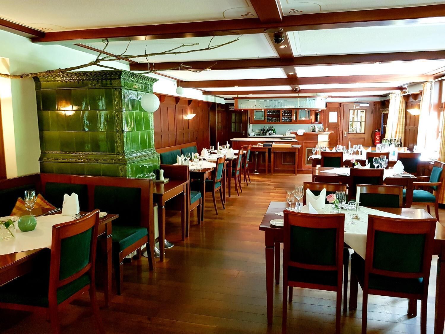 Un restaurant avec des banquettes et des tables en bois, un coin bar et un mur décoratif vert.