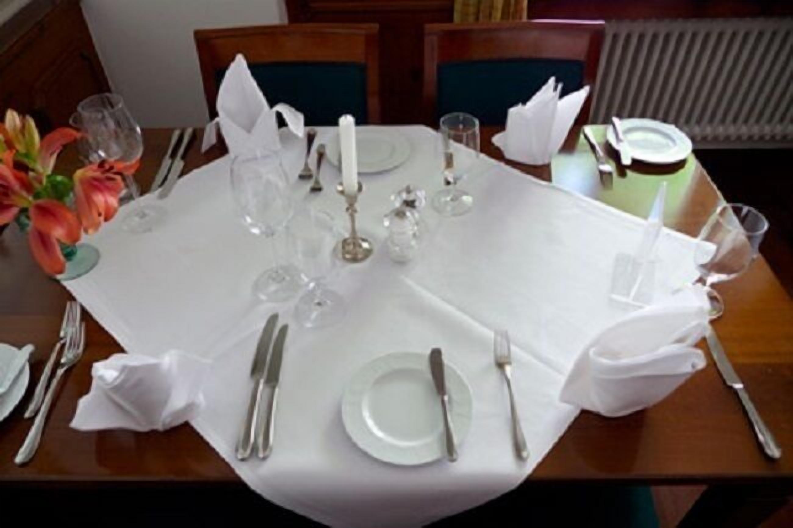 A dining table set for a meal with white tablecloth, plates, cutlery, and glassware.