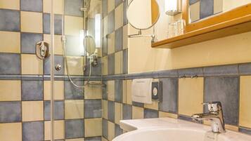 A bathroom with a checkered tile wall, a glass shower enclosure, a sink with a mirror, and a towel dispenser.