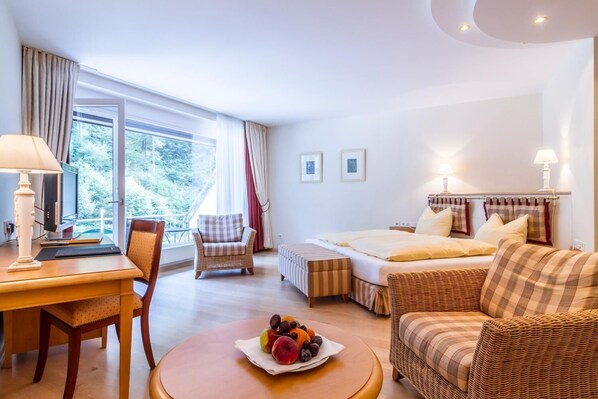 A hotel room with a bed, a desk, a chair, a sofa, and a table with fruit. - Waldhotel Bad Sulzburg (Sulzburg)