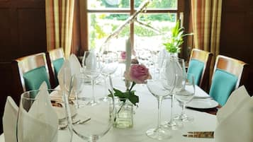 Une table à manger dressée pour un repas, avec plusieurs verres à vin, un vase contenant une rose rose et une branche décorative.