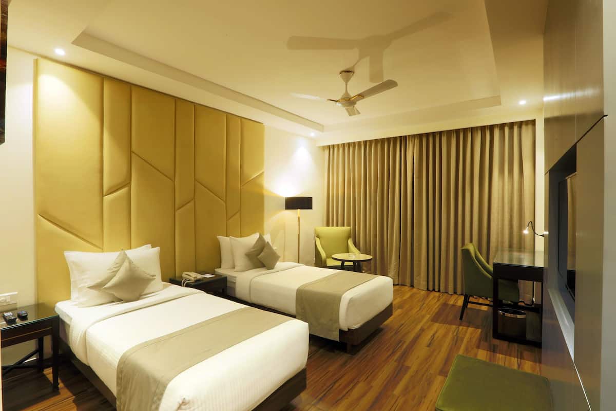 A hotel room with two beds, a desk, a chair, a TV, and a ceiling fan.