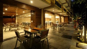 An outdoor dining area with multiple tables and chairs, a covered section with a glass wall, and potted plants. - Resort The Lohias (Candolim)