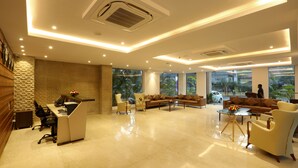 A modern hotel lobby with a reception desk, seating area, and large windows offering views of the outdoors. - Resort The Lohias (Candolim)
