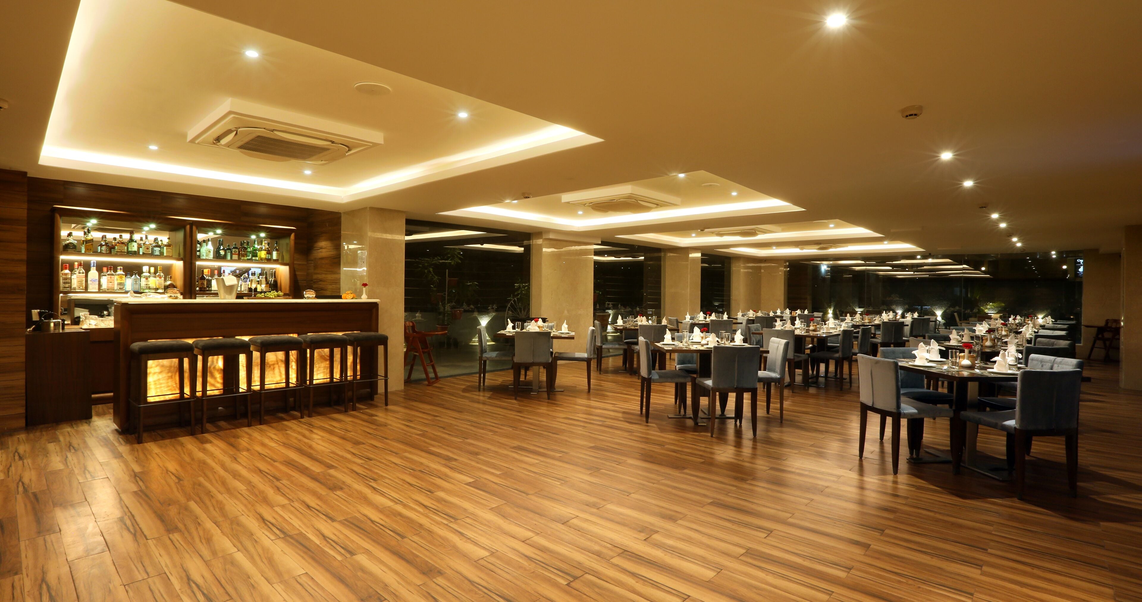 A spacious restaurant with wooden flooring, a bar area, and multiple dining tables and chairs.