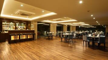 A spacious restaurant with wooden flooring, a bar area, and multiple dining tables and chairs.