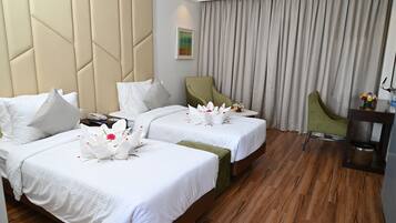 A hotel room with two beds, a green armchair, a small table with a vase of flowers, and a wooden floor.