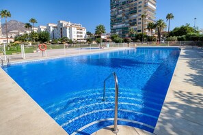 A swimming pool with a metal ladder, surrounded by a fence, and buildings in the background.
