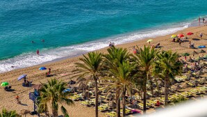 Una playa con filas de tumbonas y sombrillas, palmeras y una vista despejada del océano.