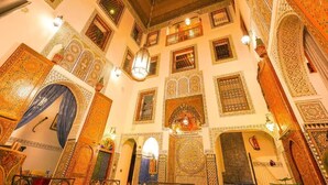 An interior with ornate arches, intricate tile work, and a high ceiling with a skylight. - Riad Sahraui (Fes)