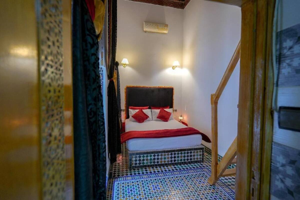 Quarto com cama, duas luminárias fixadas na parede, ar condicionado e piso estampado.