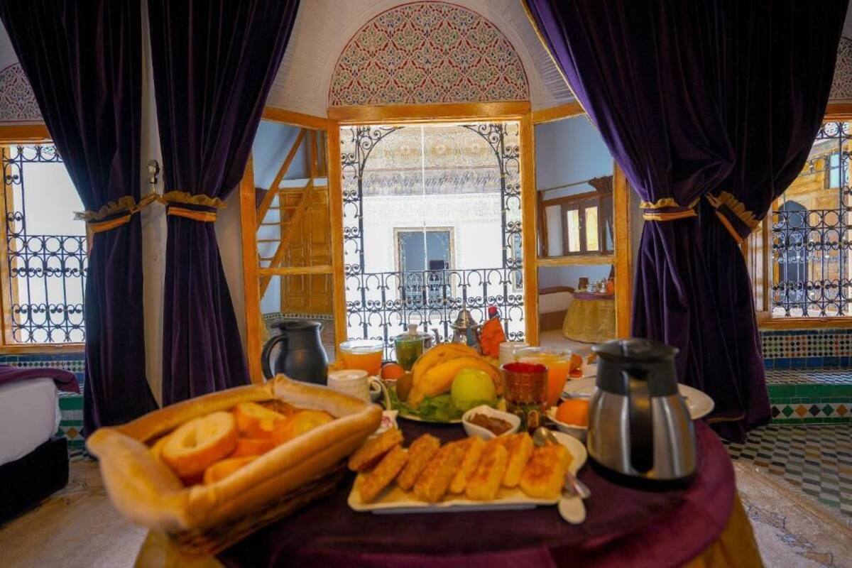 Uma área de refeições com mesa posta para o café da manhã, com pão, doces e uma cafeteira.