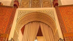 A staircase with intricate tile work and a wooden handrail leading to a room with a chair and a small table. - Riad Sahraui (Fes)