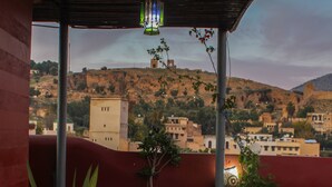 A balcony with a view of a cityscape, including buildings and a hill. There are potted plants and a table with a lamp. - Riad Sahraui (Fes)