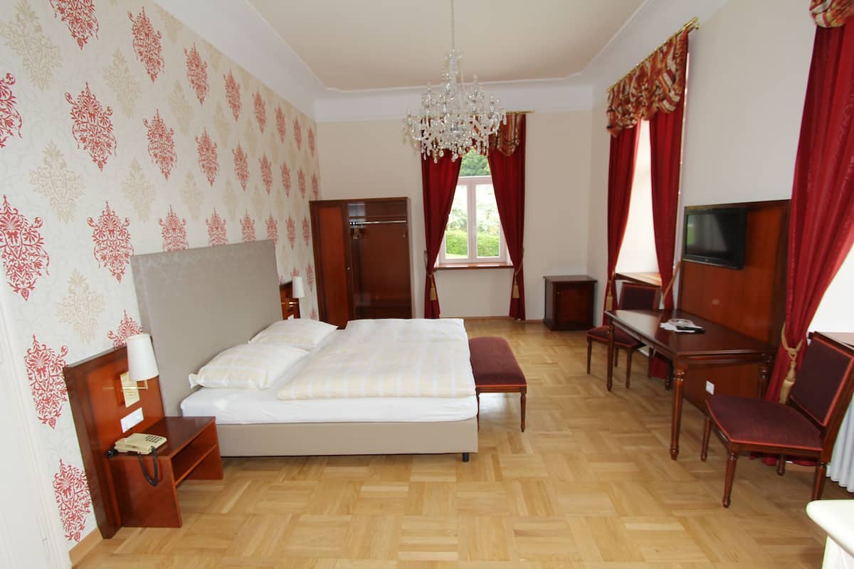 A hotel room with a large bed, a desk with a chair, a television, and a chandelier.