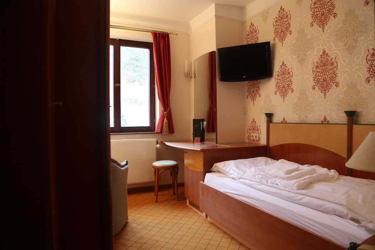 A hotel room with a bed, a desk, a television, and a window with curtains.