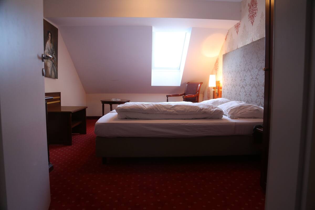 A bedroom with a bed, a chair, a desk, and a window.